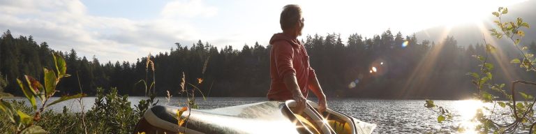 Man standing with a canoe on the shore of a lake