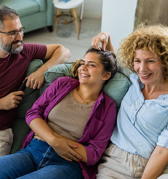 Parents are sitting with their daughter on the bed