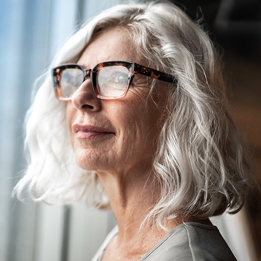 A gray-haired woman in glasses looks out the window