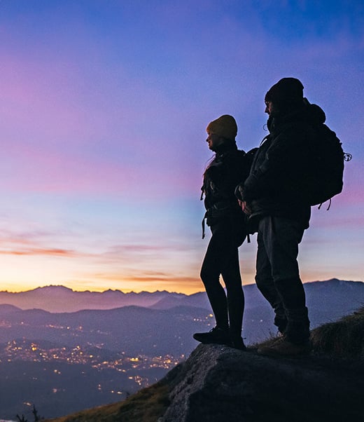 Two hikers high up looking down a city by the sea