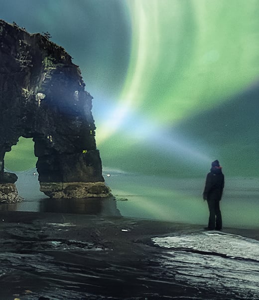 Person looking at rock formation and northern lights